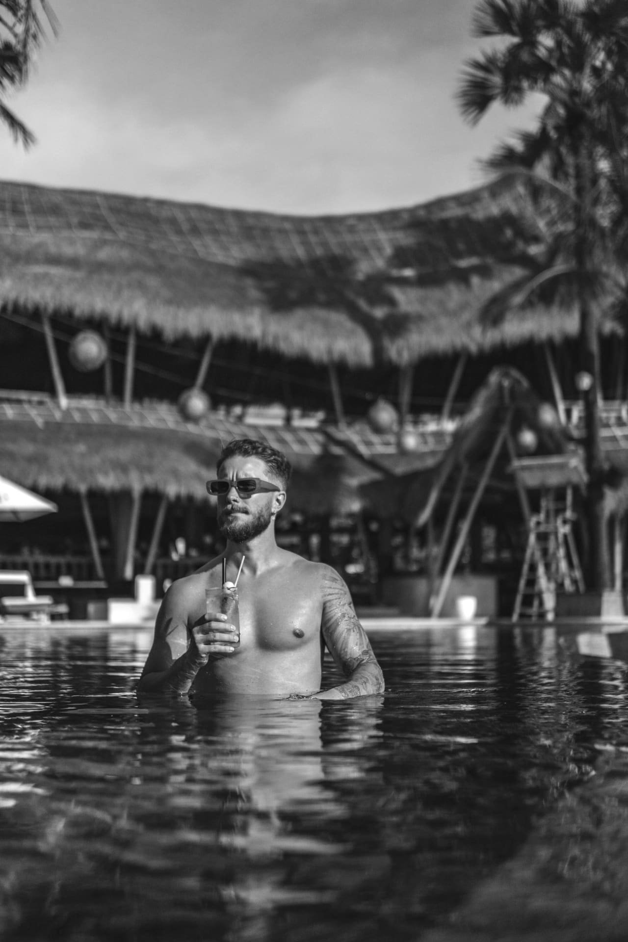 Portrait of Marvin Meyer in a pool in front of a thatched pavilion.
